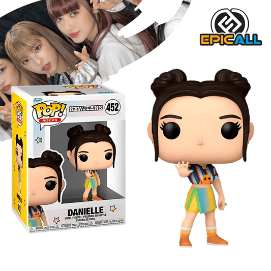 Un Funko POP de Danielle de NewJeans. La figura tiene el pelo largo y ondulado con un flequillo, un top corto blanco con un diseño, y pantalones de mezclilla o vaqueros. Tiene una expresión dulce y los ojos grandes y redondos, característicos de los Funko POP. La caja del Funko POP se ve detrás de la figura.