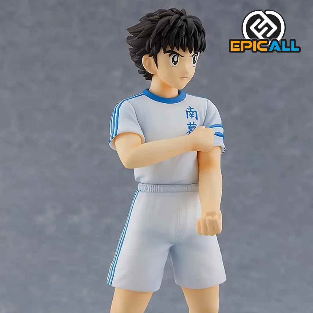 Una figura de acción de Oliver Atom, el protagonista del anime Captain Tsubasa. Oliver Atom está representado con su uniforme de fútbol azul y blanco, realizando un gesto de patear un balón. Tiene una expresión determinada y una postura atlética. La figura está colocada sobre una base que representa un campo de fútbol.