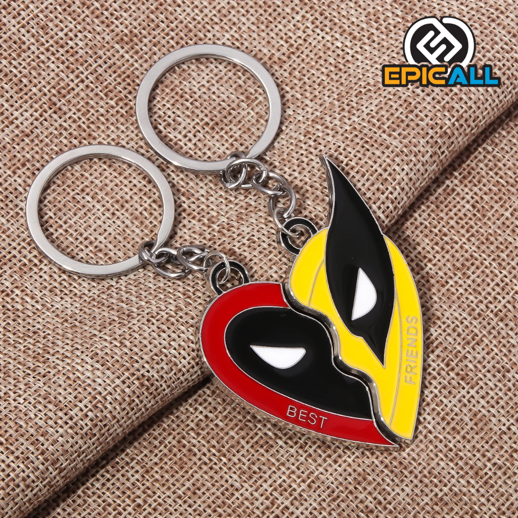 La imagen muestra dos llaveros metálicos de "Best Friends" con los personajes Wolverine y Deadpool. El llavero de Deadpool es rojo y negro, mide 5 cm x 2.5 cm, y tiene la palabra "BEST". El llavero de Wolverine es amarillo y negro, mide 6 cm x 2.6 cm, y tiene la palabra "FRIENDS". Ambos llaveros están unidos a una anilla para llaves.