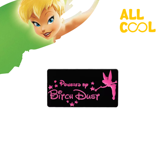 Un pin metálico rectangular con la frase "Powered by Bitch Dust" escrita en rosa sobre un fondo negro. A la derecha, se ve la silueta de un hada en rosa. El pin tiene un diseño llamativo y un acabado brillante.