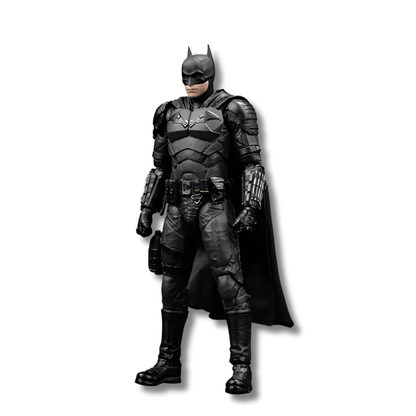 Una figura de acción articulada de Batman, basada en la película The Batman de Robert Pattinson, de unos 18 cm de alto. El personaje está de pie, con el traje blindado de color negro y una larga capa negra que cae a un lado.