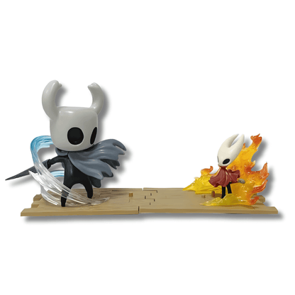 Una figura de estatua que representa una escena de duelo del videojuego Hollow Knight. En el lado izquierdo está el Caballero (The Knight), un personaje gris y negro con cuernos, atacando con efectos de energía azul claro. A la derecha está Hornet, un personaje más pequeño en traje rojo, rodeada de efectos de fuego y llamas anaranjadas.