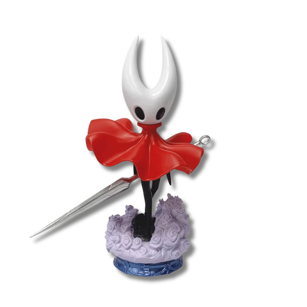Una figura de estatua del personaje Hornet del videojuego Hollow Knight, de unos 19 cm de altura. El personaje es negro con una máscara blanca con cuernos y una capa roja. Sostiene una aguja larga y delgada, y está de pie sobre una base que simula un terreno con pequeñas flores moradas.