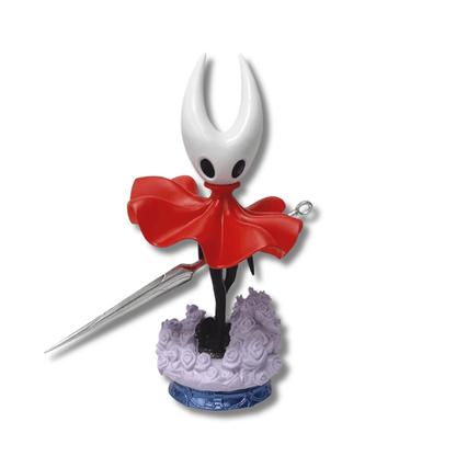 Una figura de estatua del personaje Hornet del videojuego Hollow Knight, de unos 19 cm de altura. El personaje es negro con una máscara blanca con cuernos y una capa roja. Sostiene una aguja larga y delgada, y está de pie sobre una base que simula un terreno con pequeñas flores moradas.