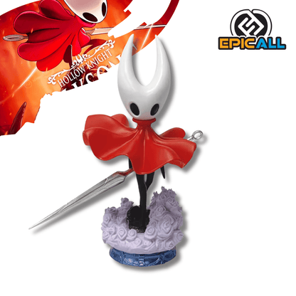 Una figura de estatua del personaje Hornet del videojuego Hollow Knight, de unos 19 cm de altura. El personaje es negro con una máscara blanca con cuernos y una capa roja. Sostiene una aguja larga y delgada, y está de pie sobre una base que simula un terreno con pequeñas flores moradas.