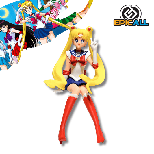 Una figura de estatua de Sailor Moon (Serena Tsukino), de unos 15 cm de altura, en su uniforme de marinera rojo, blanco y azul con botas rojas y coletas rubias largas. La figura está sentada y tiene una mano levantada haciendo el signo de la paz.
