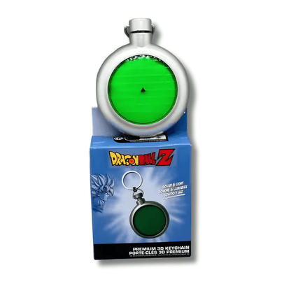 Llavero circular que representa el Radar de las Esferas del Dragón de la serie Dragon Ball. El dispositivo es de color plateado con una pantalla central circular de color verde brillante que muestra una cuadrícula y un pequeño triángulo negro indicativo. Debajo del radar se observa su caja de empaque azul con el logotipo de Dragon Ball Z, indicando que posee funciones de luz y sonido.