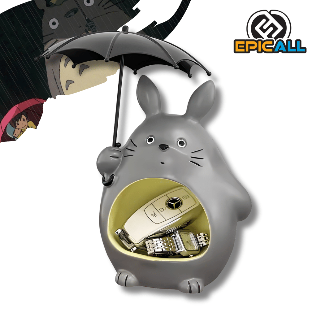 Un organizador con la forma del personaje de Totoro de color gris, sosteniendo un paraguas negro. El abdomen de Totoro tiene una abertura circular de color amarillo claro, donde se pueden colocar llaves, un reloj y un llavero de auto, visibles en la imagen.