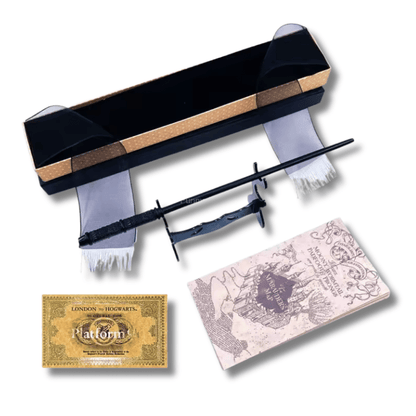 Fotografía de un set de coleccionista de Harry Potter sobre un fondo blanco. El set incluye una varita negra detallada reposando sobre un soporte negro, una réplica del Mapa del Merodeador, un ticket dorado de la Plataforma 9 3/4 "London to Hogwarts" y una caja de regalo negra y dorada con listones de tul blanco y negro.